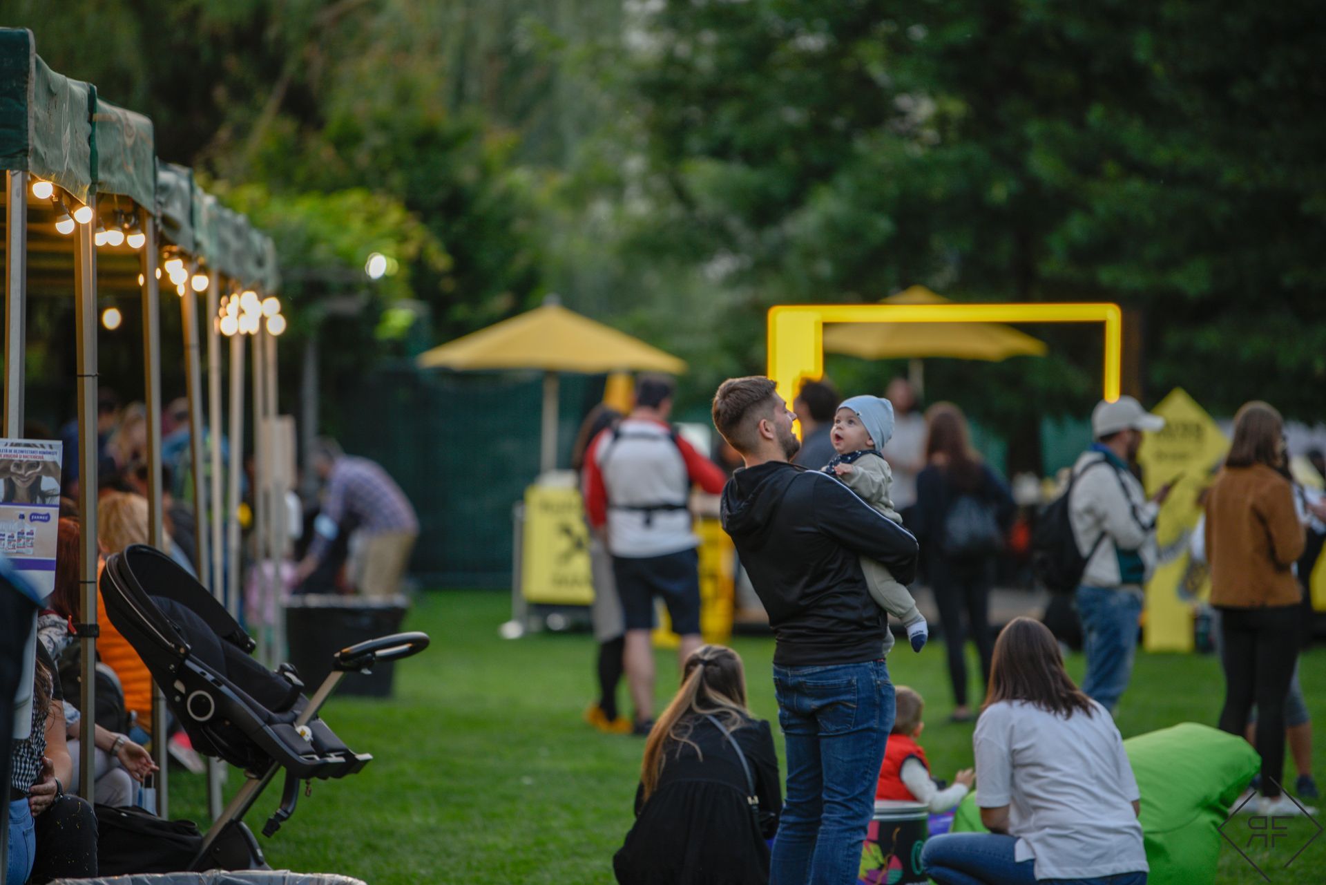 La gente se reunió en un evento al aire libre en un parque, con tiendas de campaña, sillas y un marco amarillo al fondo.