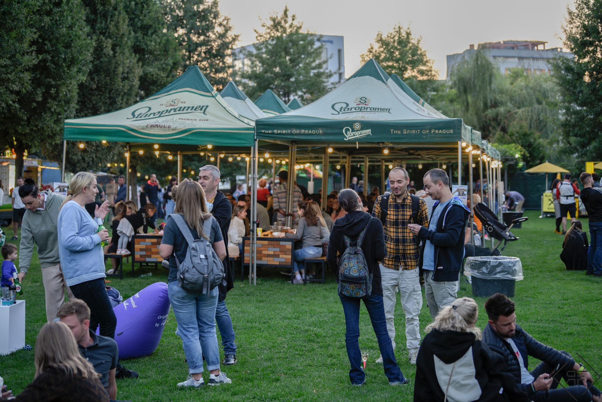 Mercado nocturno al aire libre con gente reunida alrededor de carpas verdes de vendedores en un parque.