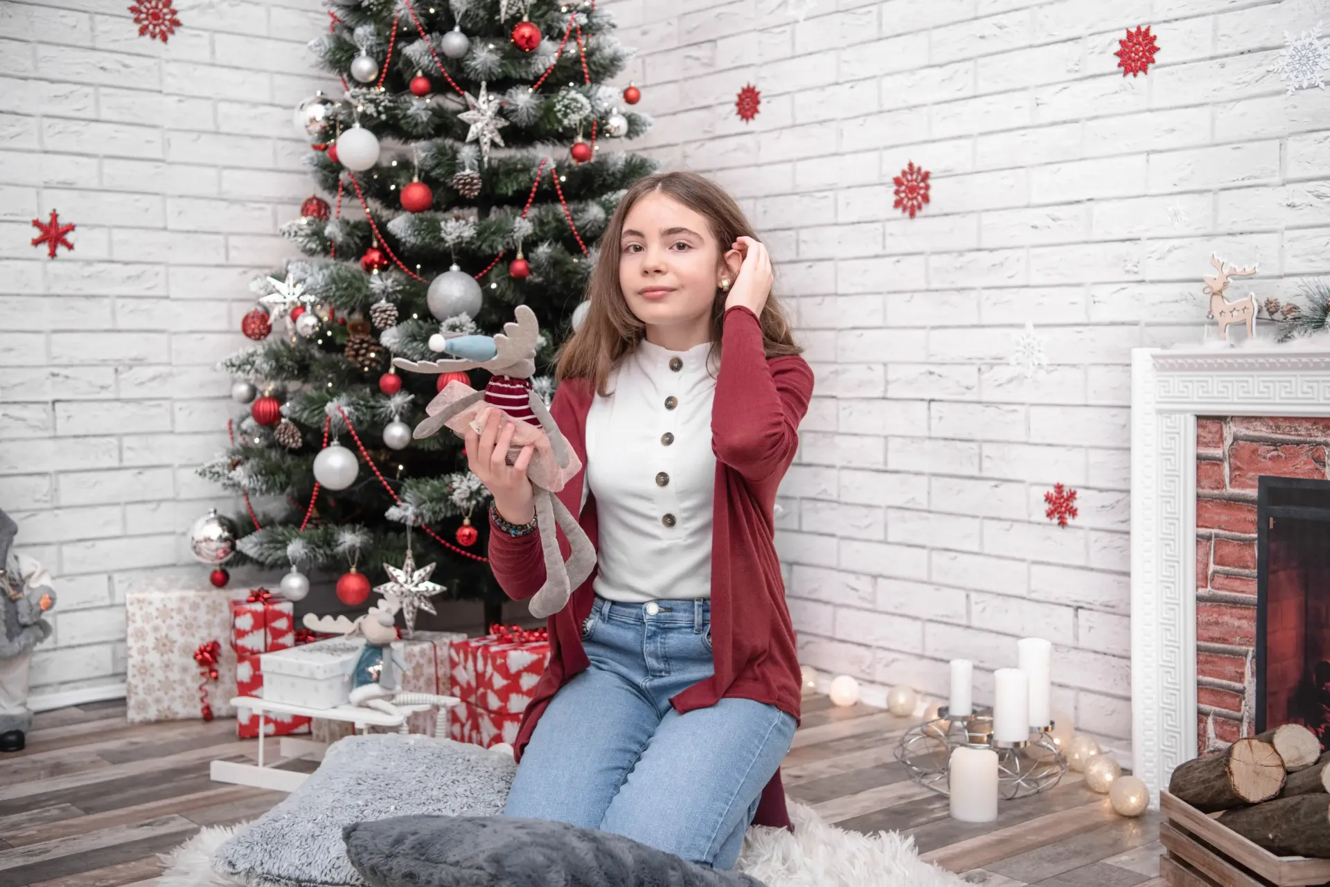 Niña sentada junto a un árbol de Navidad decorado, sosteniendo un adorno navideño en una habitación acogedora.