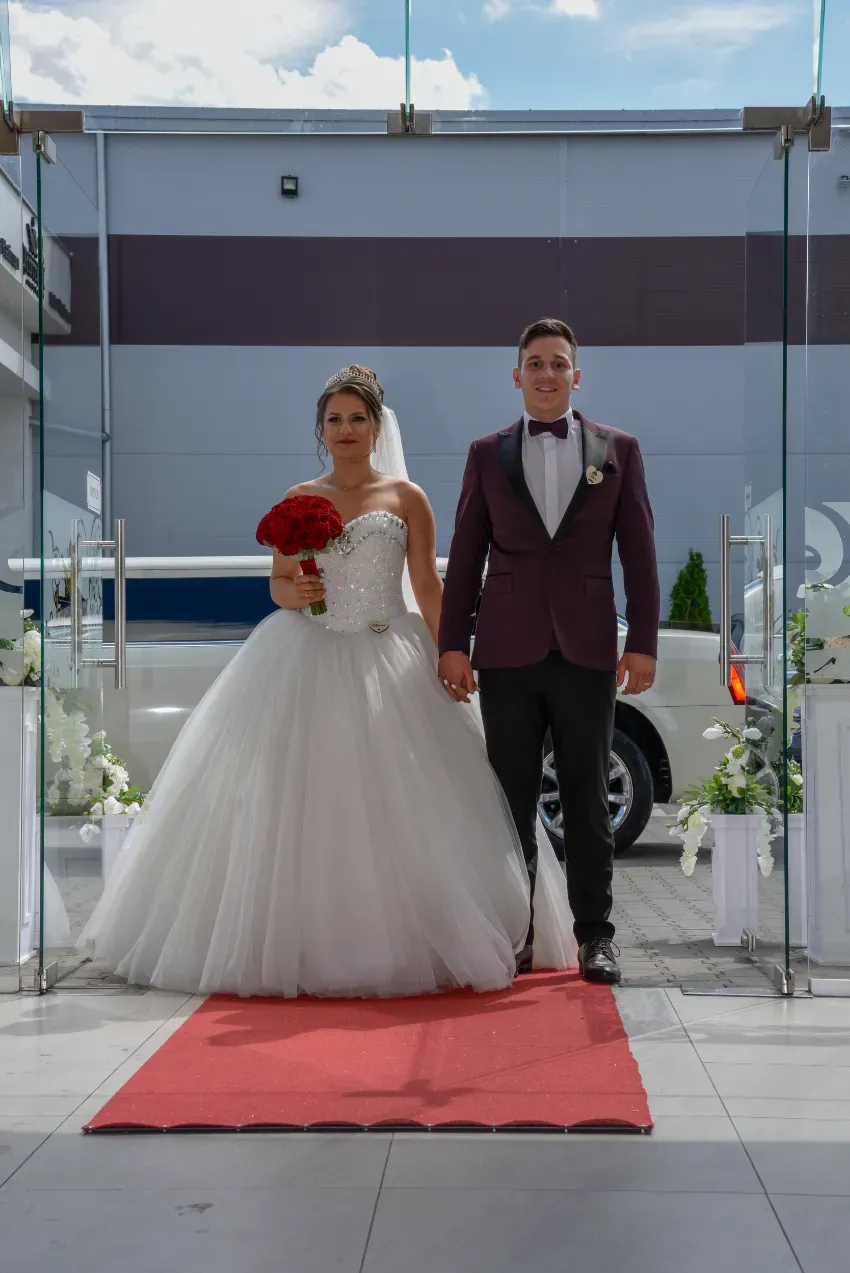 Novios de pie sobre una alfombra roja en un lugar para bodas al aire libre.
