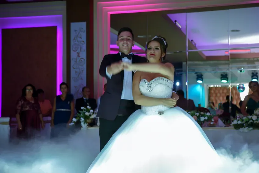 Novios bailando en un salón de recepción lleno de niebla con iluminación rosa y morada.