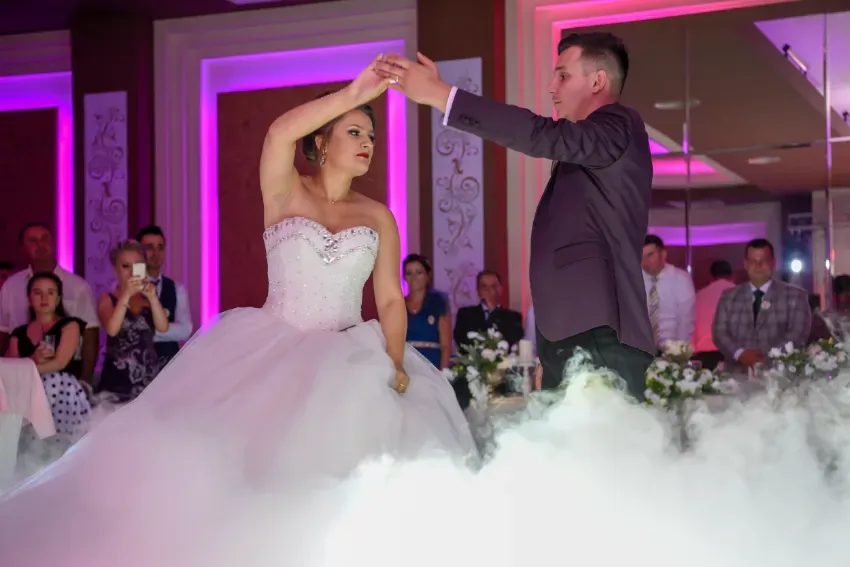 Novios bailando bajo luces rosas con niebla en el suelo en una recepción de boda.