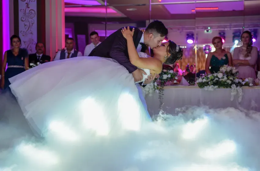 Los recién casados ​​se besan en una pista de baile cubierta de nubes en una recepción nupcial iluminada con luces moradas.