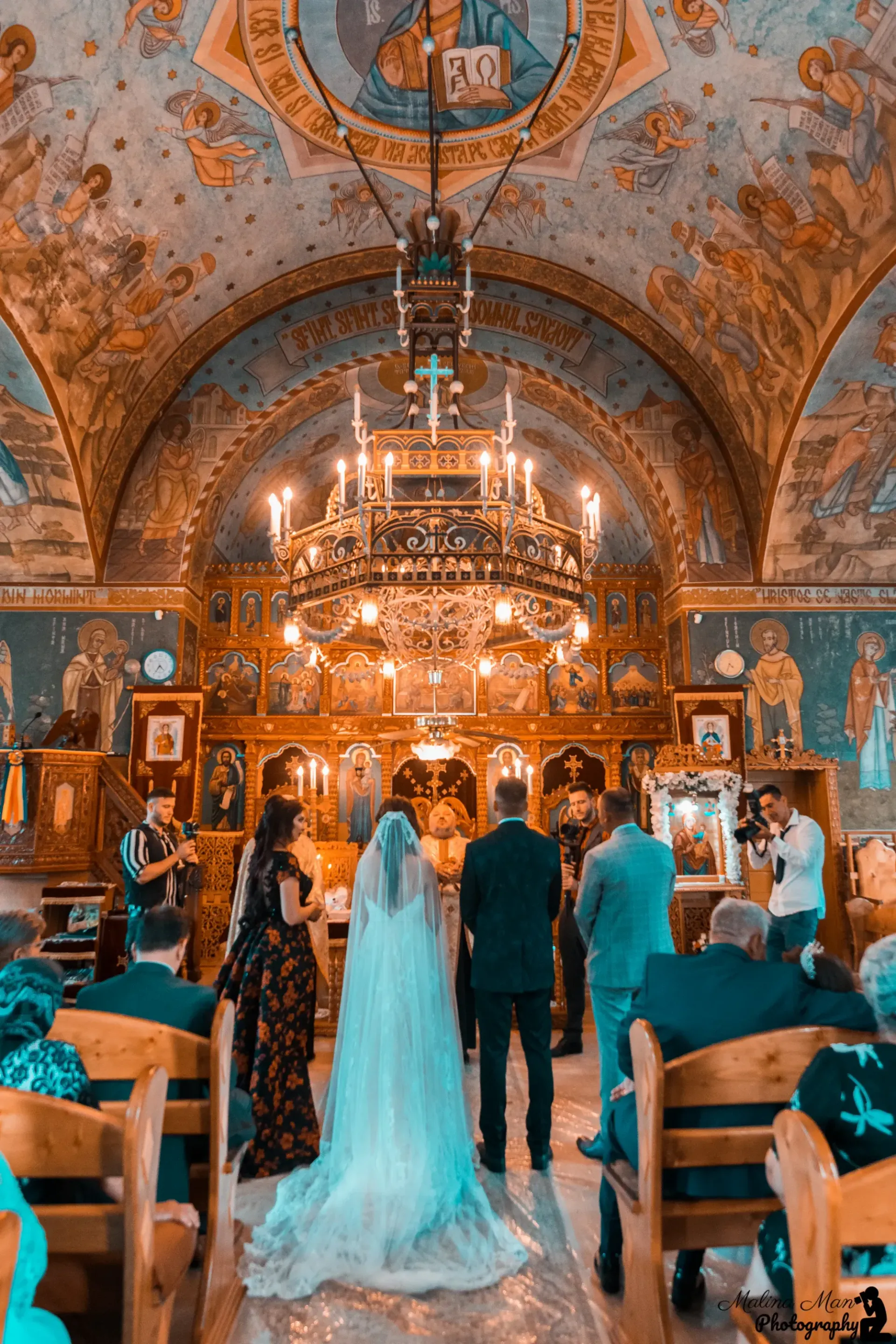 Una pareja se encuentra en una iglesia ricamente decorada, frente a un altar dorado ornamentado, durante una ceremonia nupcial.