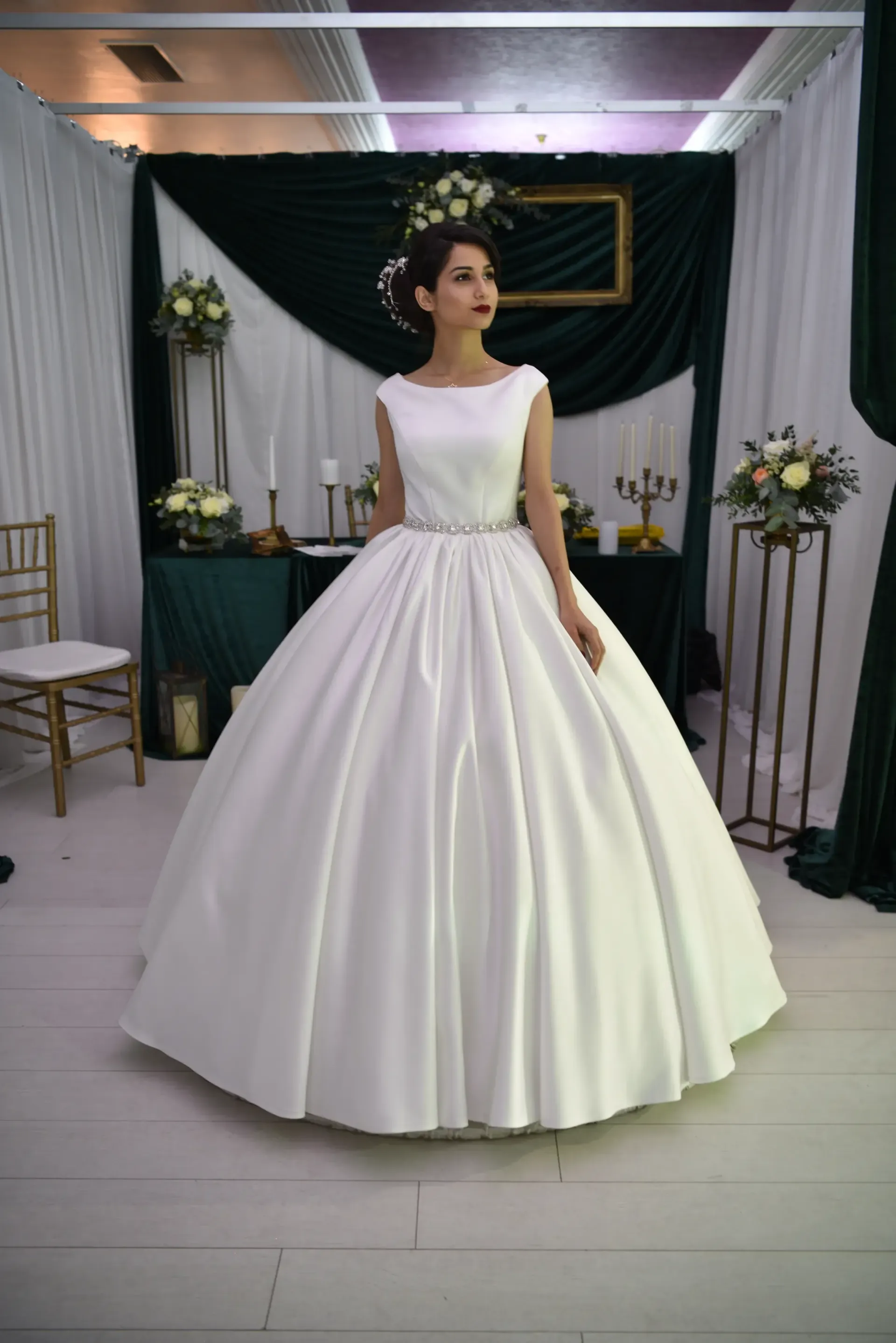 Mujer con vestido de gala blanco de pie en un espacio interior decorado para eventos.