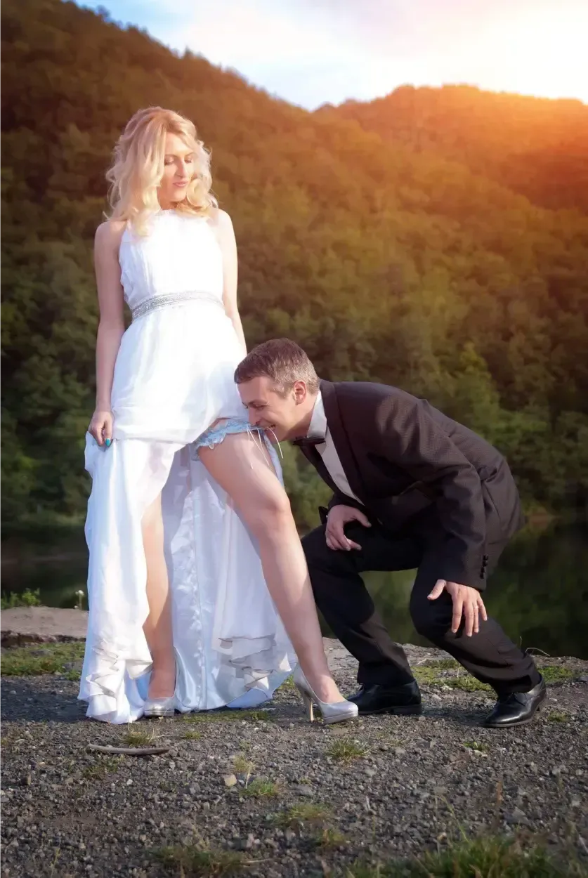 Los novios posan al aire libre al atardecer, con el novio arrodillado junto al vestido de ella.