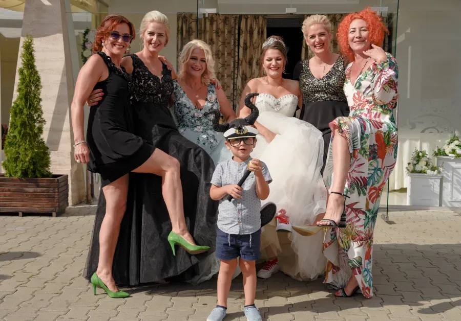 Grupo posando al aire libre en una celebración, con un niño al frente y una novia con un vestido blanco.