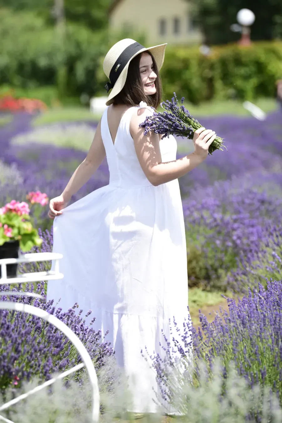 Mujer con vestido y sombrero blancos sosteniendo lavanda junto a una bicicleta blanca en un campo de flores moradas.