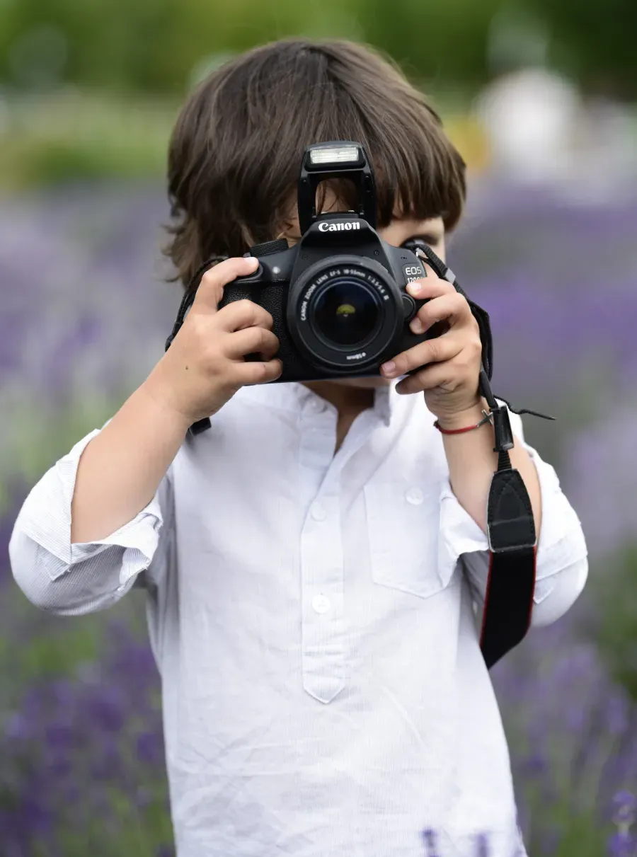 Un niño sosteniendo una cámara en un campo de flores moradas.