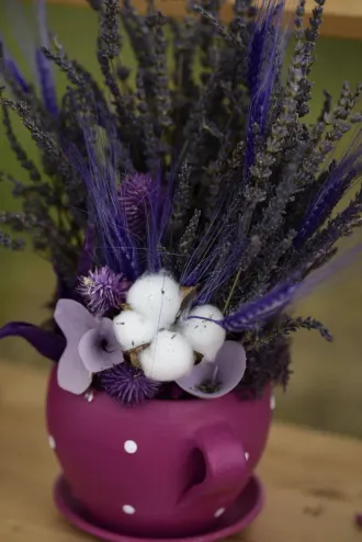 Arreglo floral morado con ramitas de lavanda y bayas blancas en un jarrón magenta con puntos blancos.