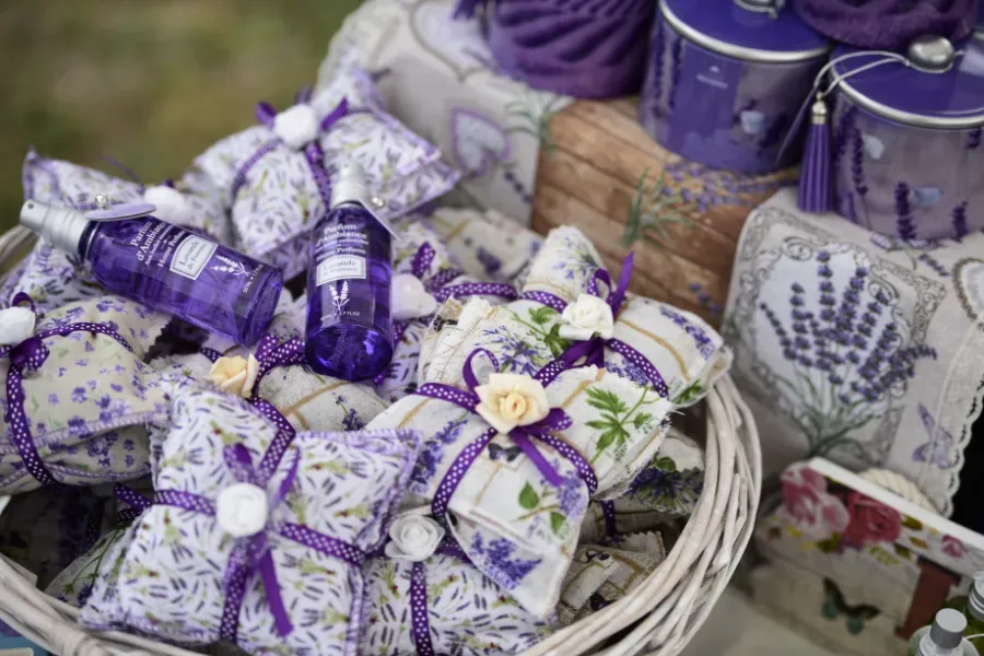 Paquetes de regalo de lavanda atados con cintas blancas en una cesta de mimbre, con artículos de tela morada a juego cerca.