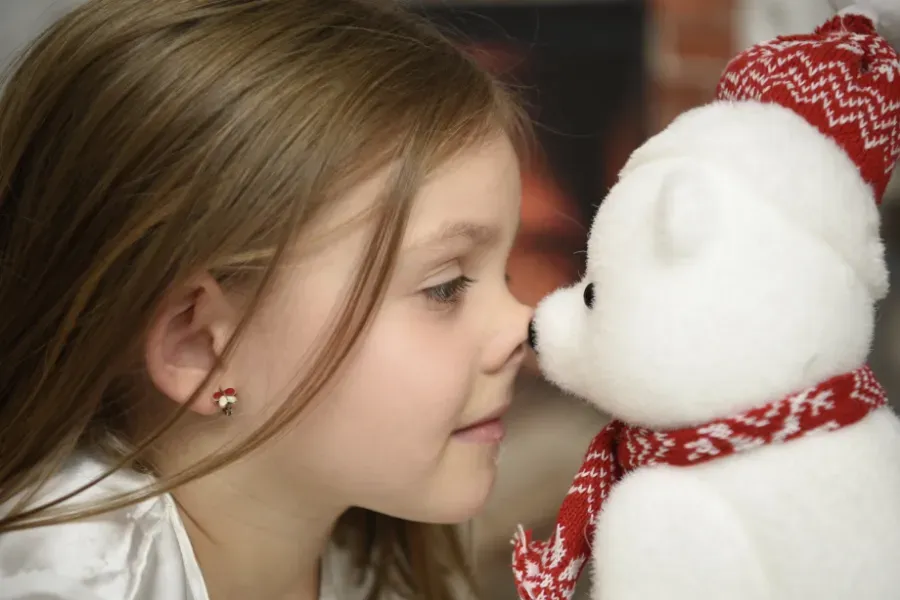 Niña tocando narices con un osito de peluche blanco que lleva una bufanda roja.