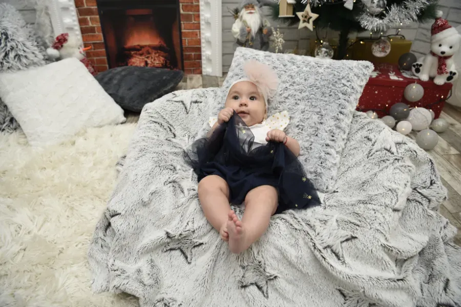Bebé tumbado sobre una manta mullida con estampado de estrellas junto a una chimenea, en un acogedor ambiente navideño.
