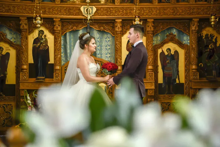 Novios tomados de la mano en una iglesia decorada, con arreglos florales en primer plano.