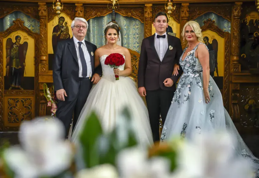 Pareja de recién casados ​​posando con dos invitados en una iglesia ornamentada; la novia, con un vestido blanco, sostiene un ramo rojo.