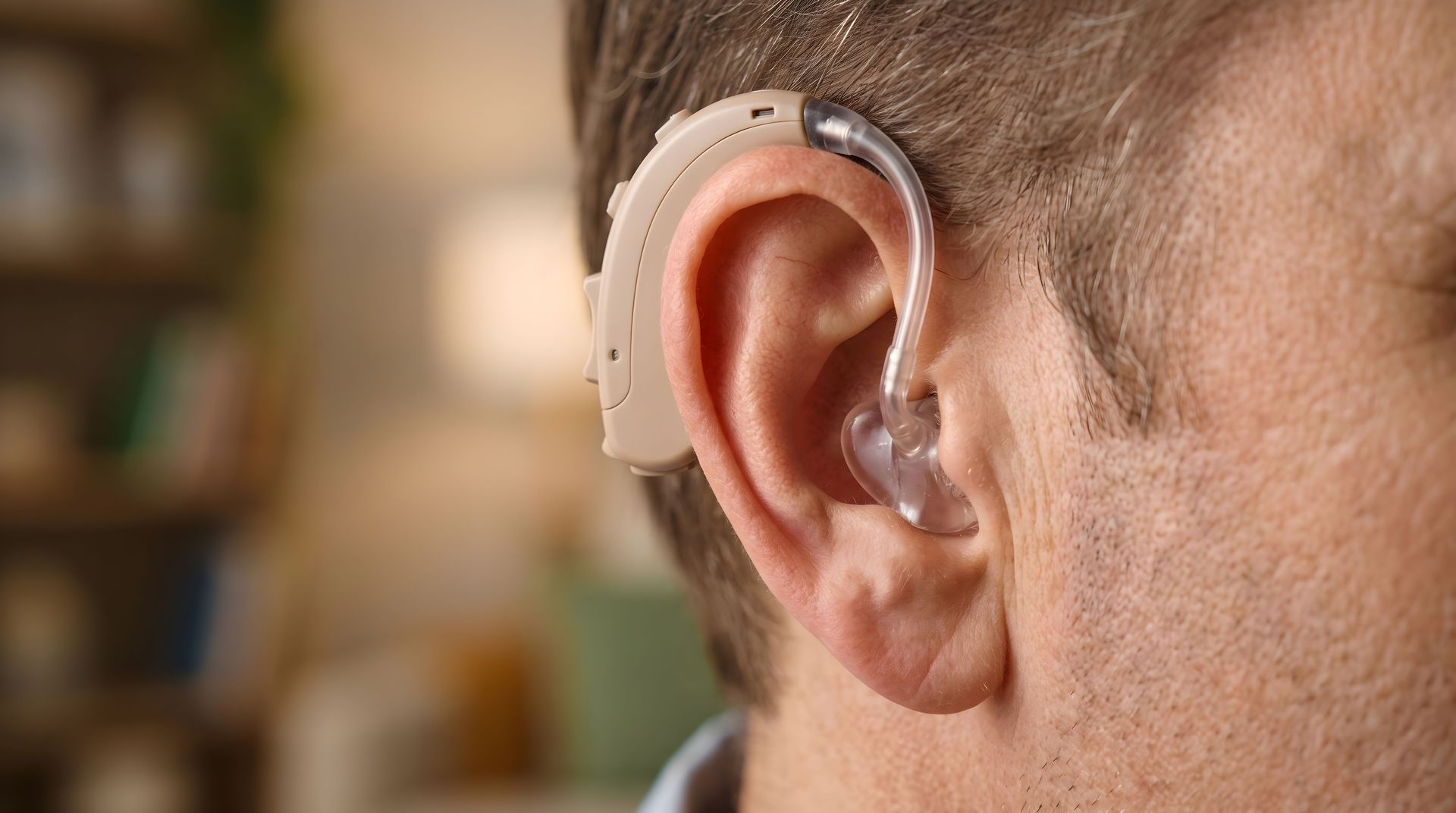 Gros plan sur un appareil auditif derrière une oreille, avec un arrière-plan intérieur flou.