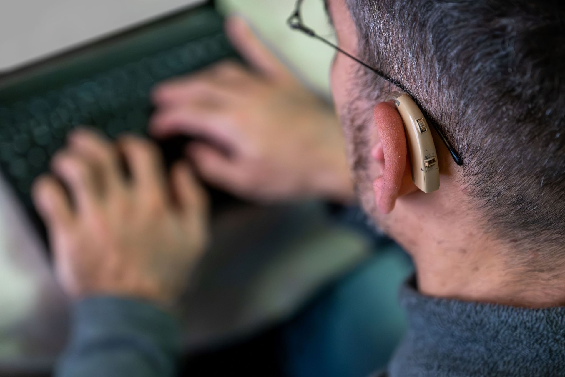 Personne en train de taper au clavier, portant une aide auditive beige à l’oreille