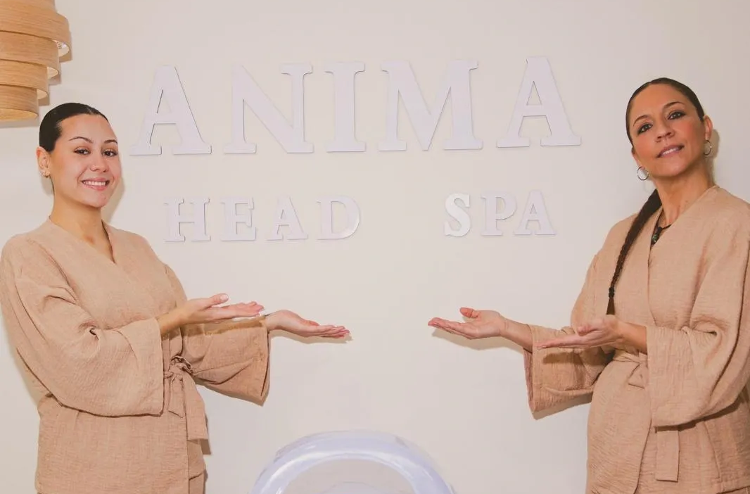 Dos mujeres con túnicas beige, haciendo gestos hacia el cartel 