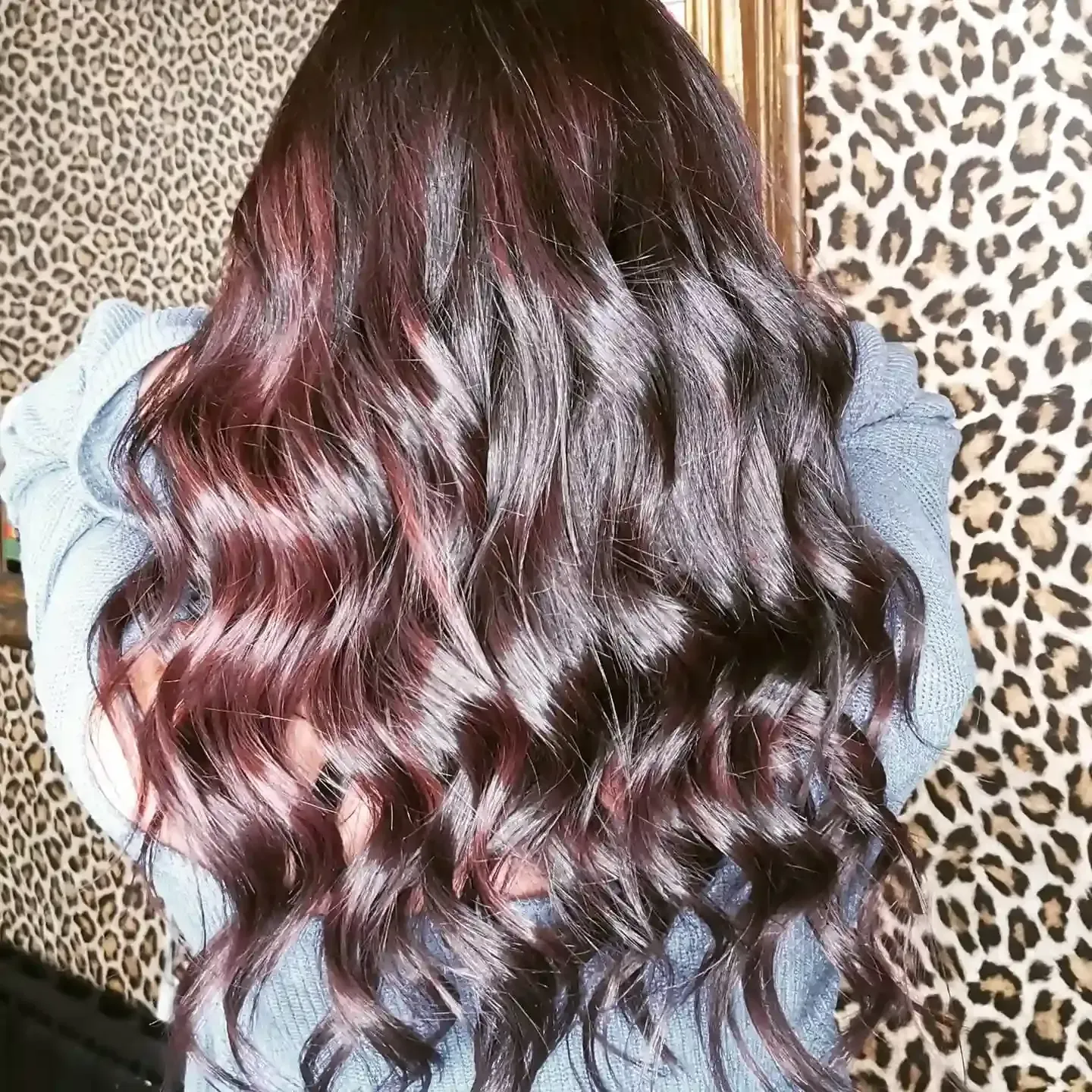 Mujer con cabello castaño rojizo largo y ondulado. Sobre un fondo con estampado de leopardo.