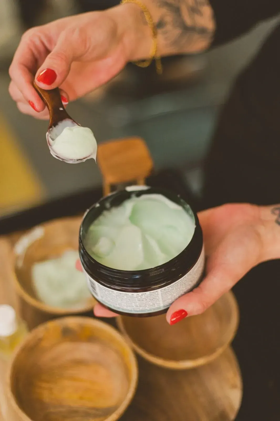 Persona sacando crema de un frasco con una cuchara de madera; hay otros recipientes de madera cerca.