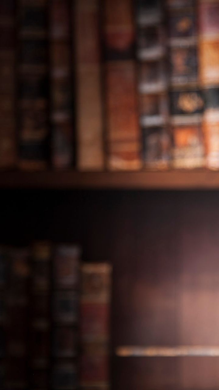 Des étagères remplies de vieux livres reliés en cuir ; un éclairage d'ambiance chaleureux.