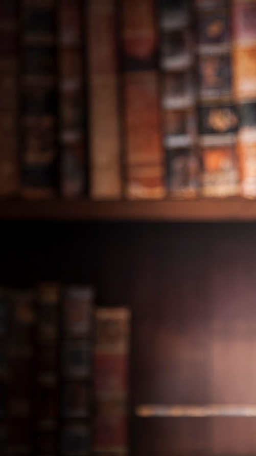 Des étagères remplies de vieux livres reliés en cuir ; un éclairage d'ambiance chaleureux.