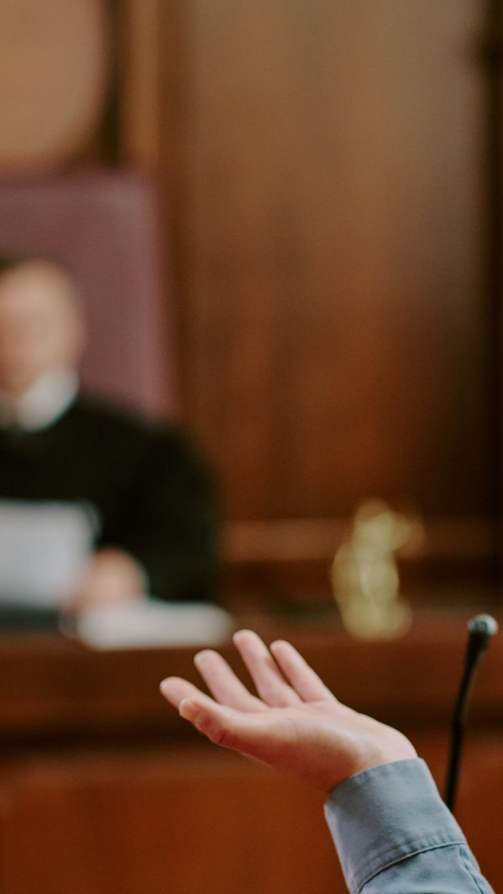 Main levée dans une salle d'audience, en direction d'un juge flou sur fond de bois.