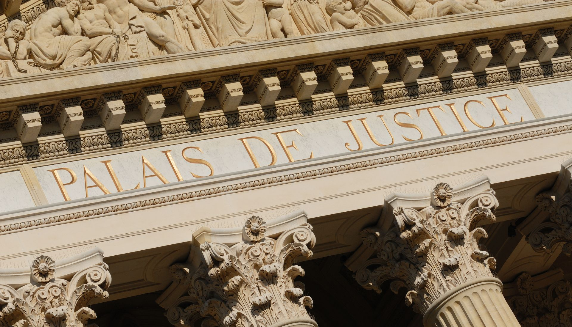 « Palais de Justice » en lettres d'or sur un bâtiment classique en pierre avec des colonnes et des sculptures ornementées.