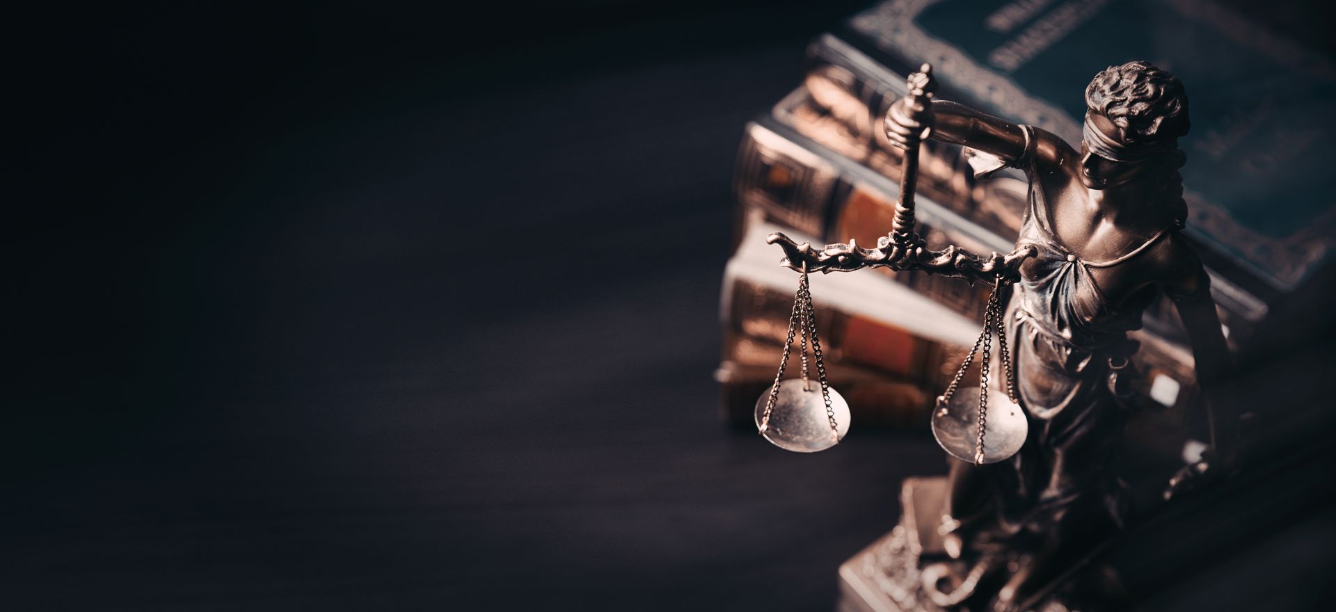 Statue de la Dame Justice avec une balance, à côté de livres, sur une surface sombre.