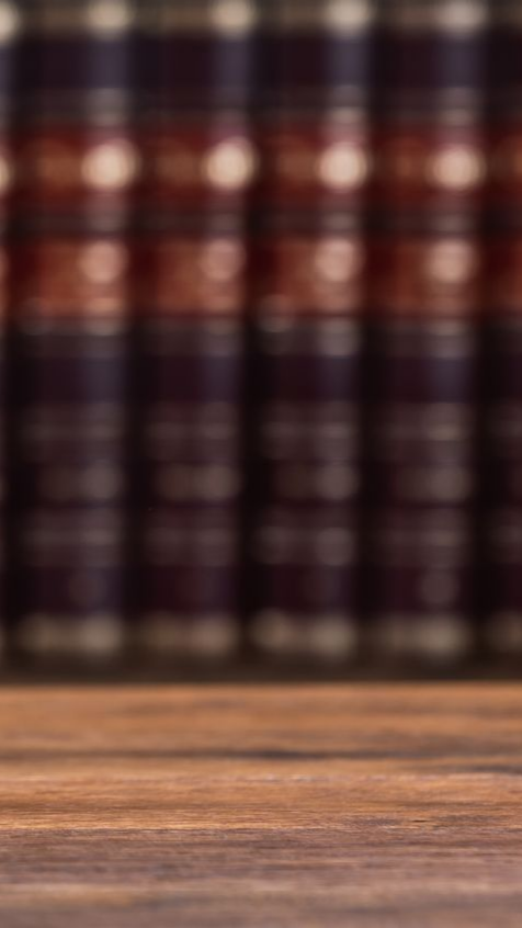 Surface en bois devant un fond flou composé de grands livres sombres aux accents rouges et dorés.