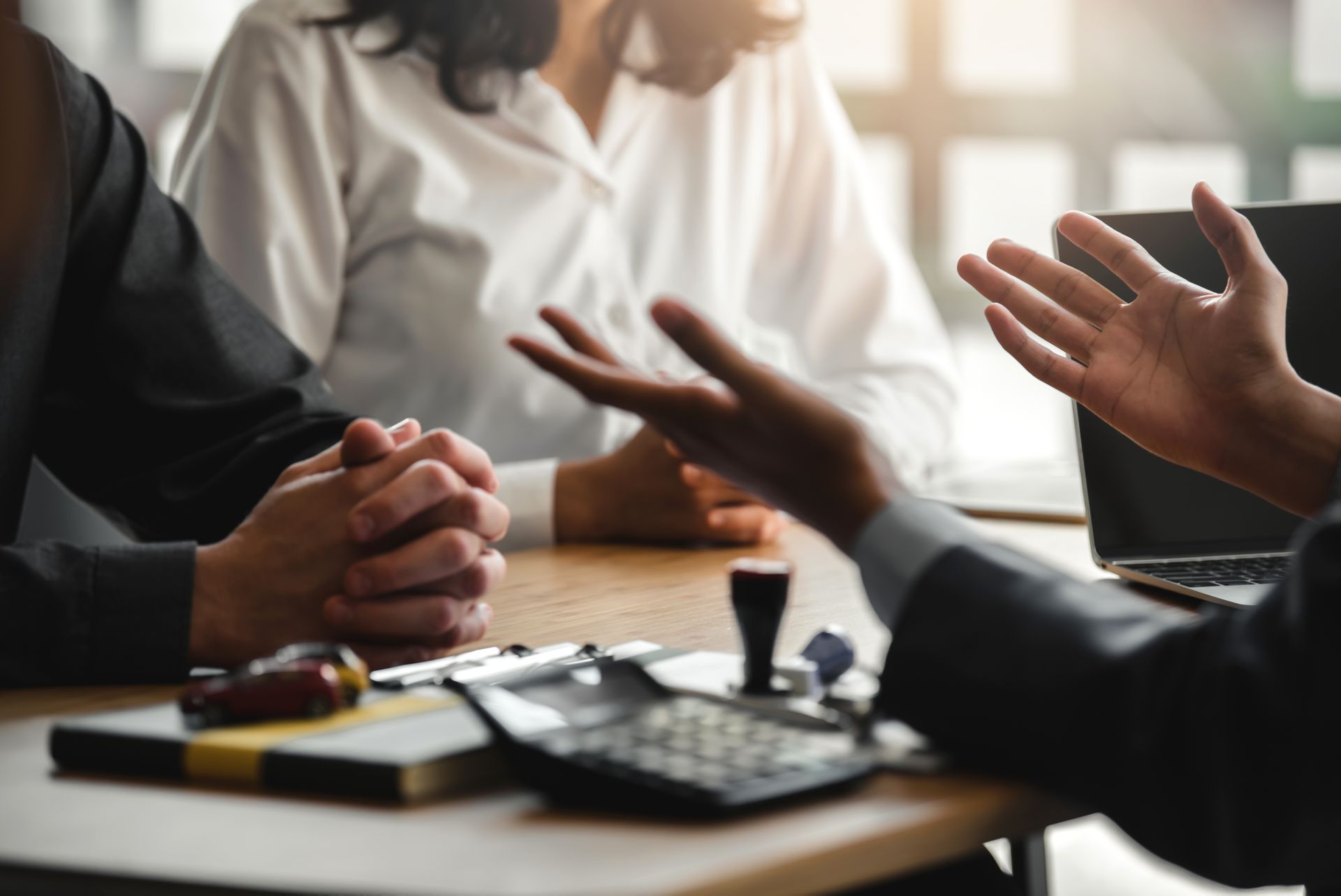 Une personne désigne la table du doigt, discute avec un couple, des documents et une calculatrice sont présents.