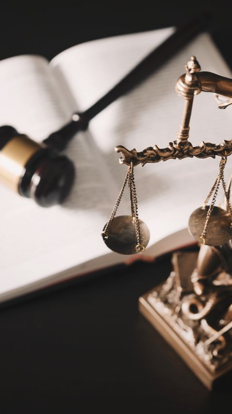 Balance de la justice, maillet et livre de lois ouvert sur une surface sombre.