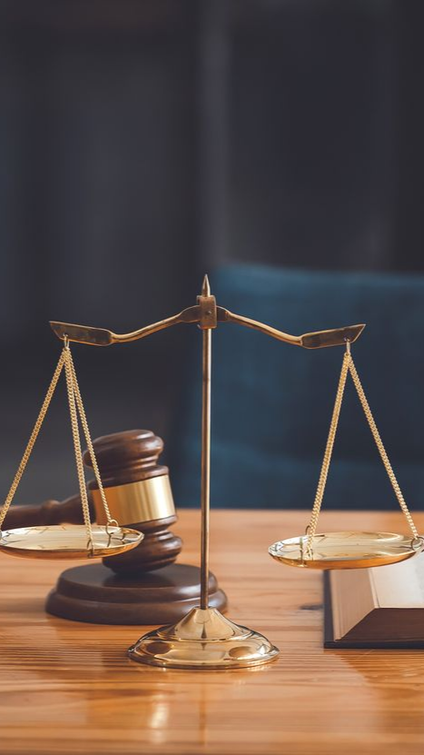 Un maillet et une balance de la justice sur un bureau en bois, avec un livre ouvert en arrière-plan.