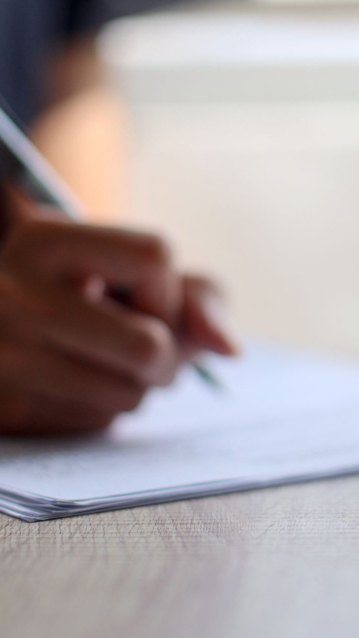 Une personne écrit sur du papier avec un stylo à une table en bois.