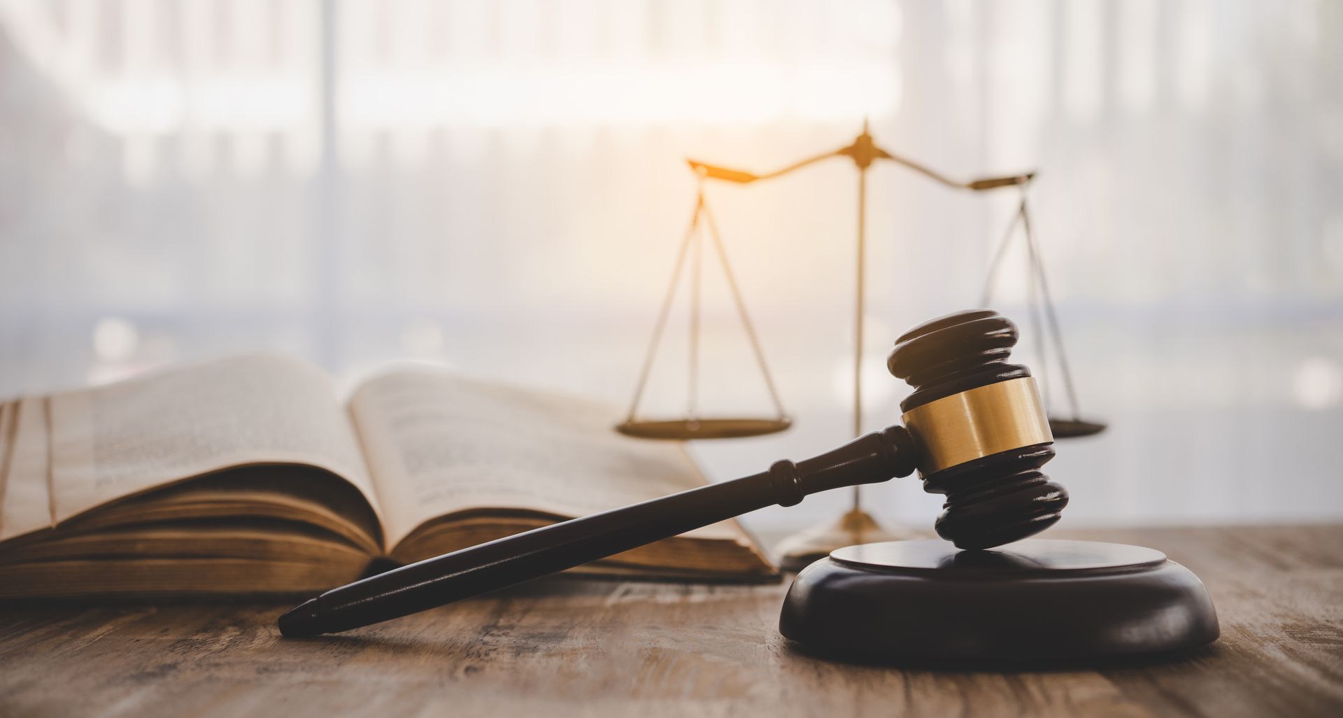 Un maillet sur son socle, devant un livre de lois et une balance de la justice, sur une table en bois.