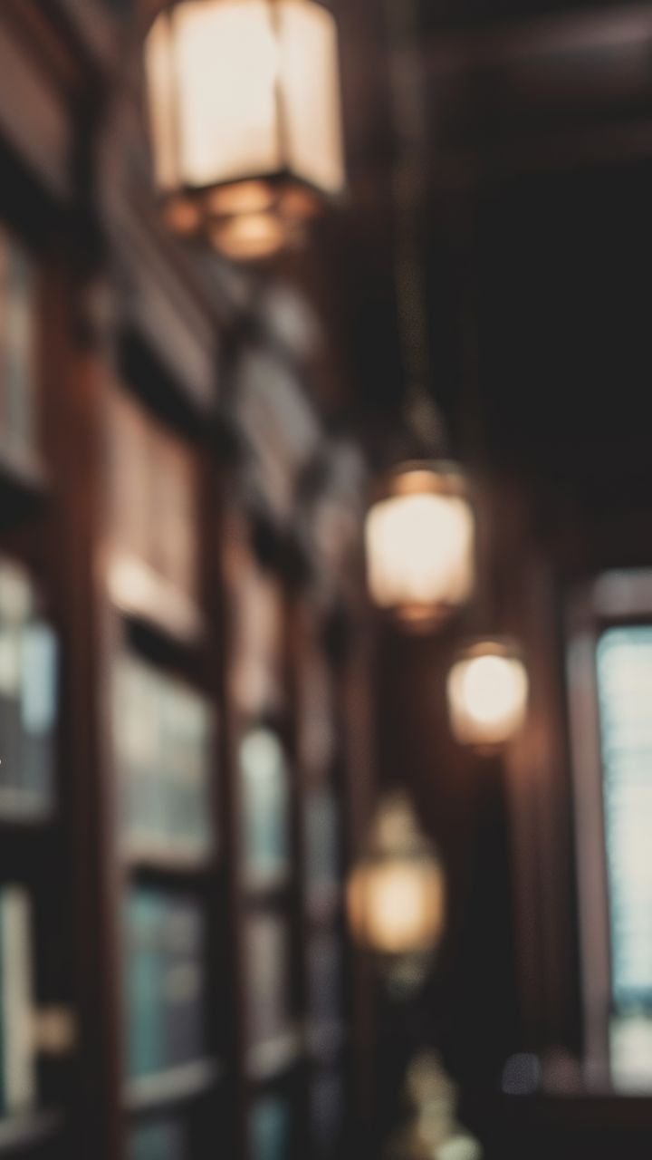 Vue floue d'une bibliothèque avec des étagères et des lampes suspendues.