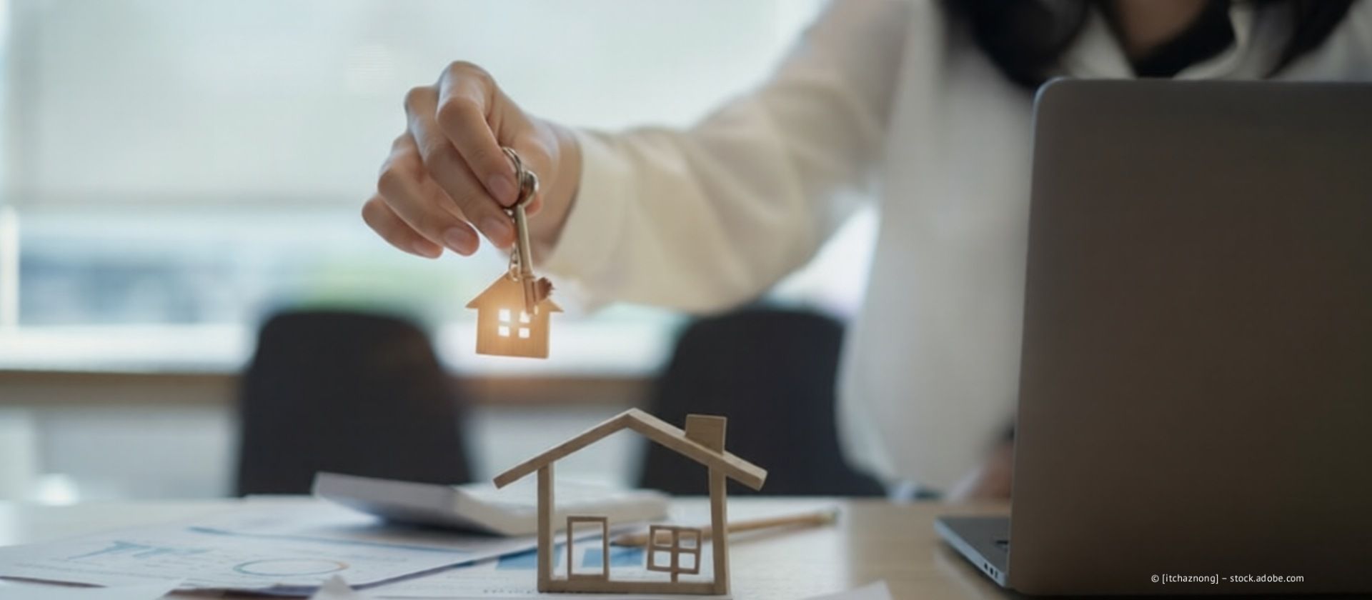 Menschen sichten Dokumente um ein Miniaturhausmodell, einen Taschenrechner, Stifte und Papiere auf einem Holztisch.