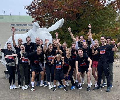 Een groep hardlopers in zwarte shirts viert hun succes voor een wit beeld en een gebouw.