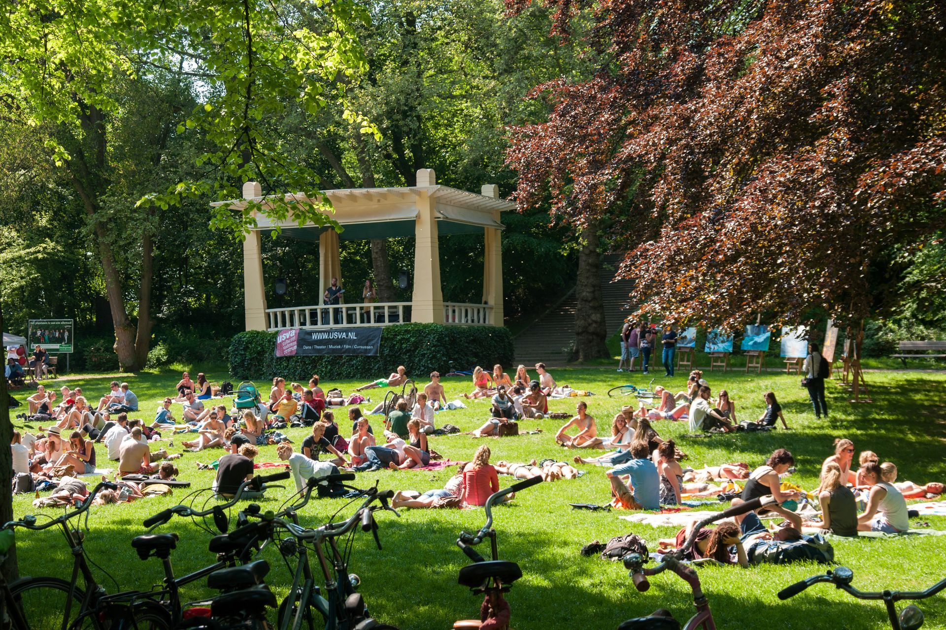 Mensen doen yoga op een grasveld voor een prieel. Fietsen staan ​​in de buurt geparkeerd. Zonnige dag.