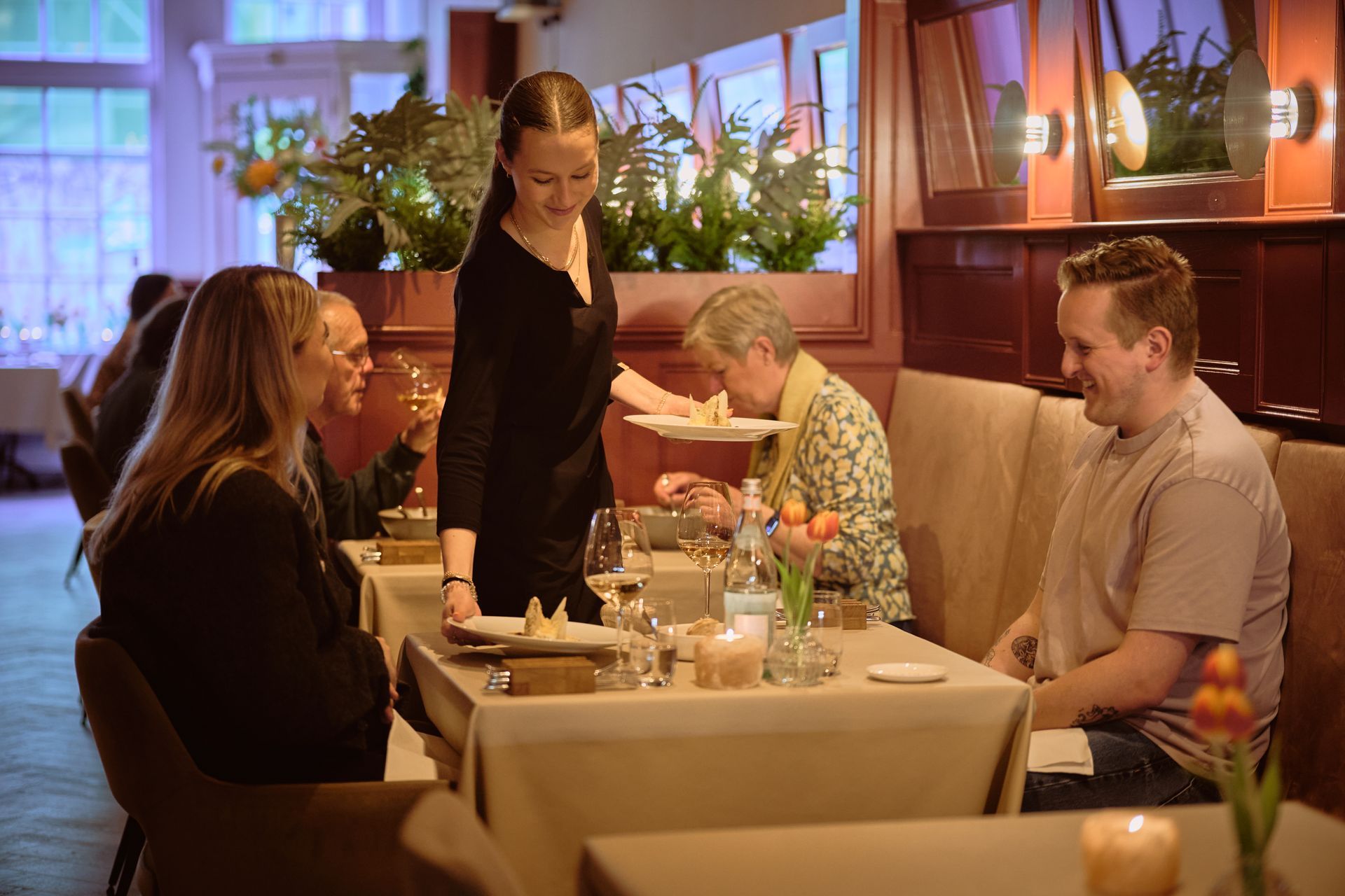 Een persoon houdt een schaal croissants vast, bij een buffet met gebak en koffie, in een keuken.