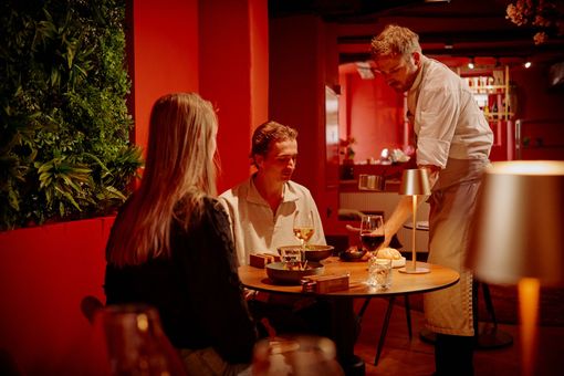 Een ober serveert wijn aan een bruidspaar aan een ronde tafel in een restaurant met rode muren.