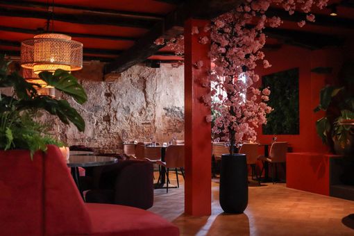 Restaurantinterieur in rode tinten met een zichtbare stenen muur, accenten met kersenbloesem en een fluwelen bank.