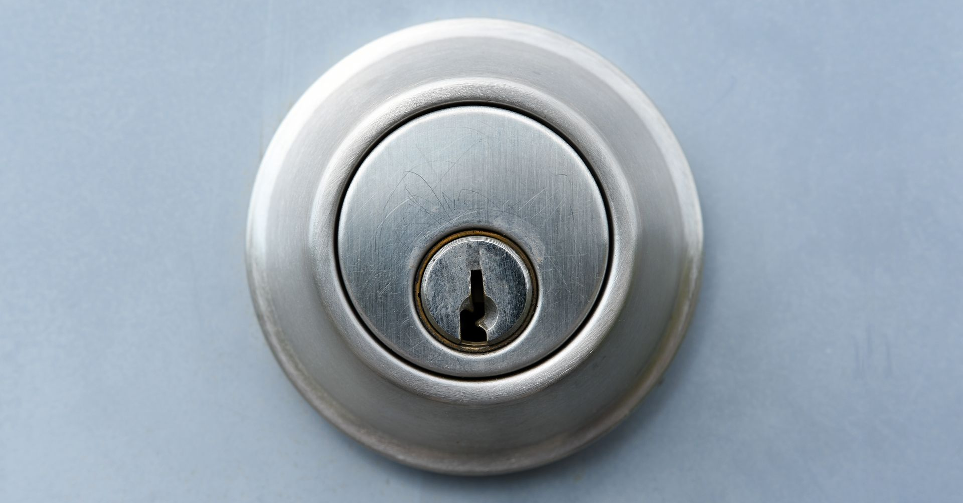 Serrure à pêne dormant argentée sur une porte grise.