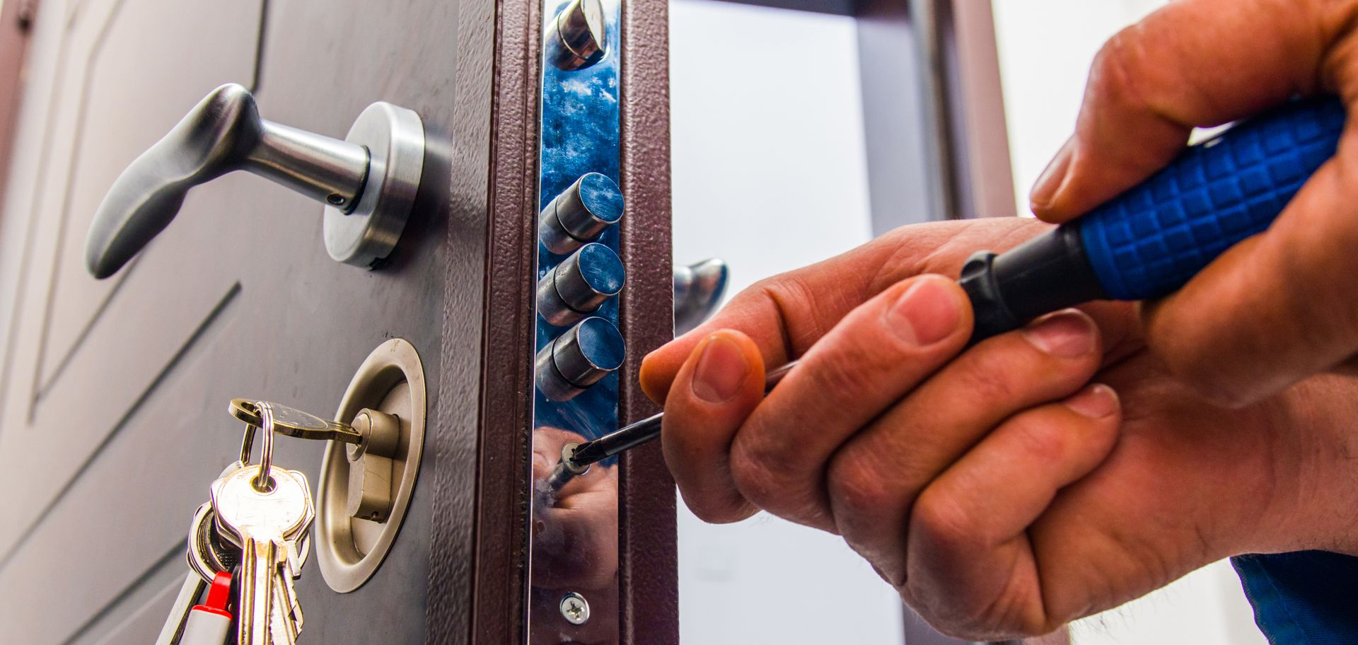 Une personne installe une serrure sur une porte marron à l'aide d'un tournevis.