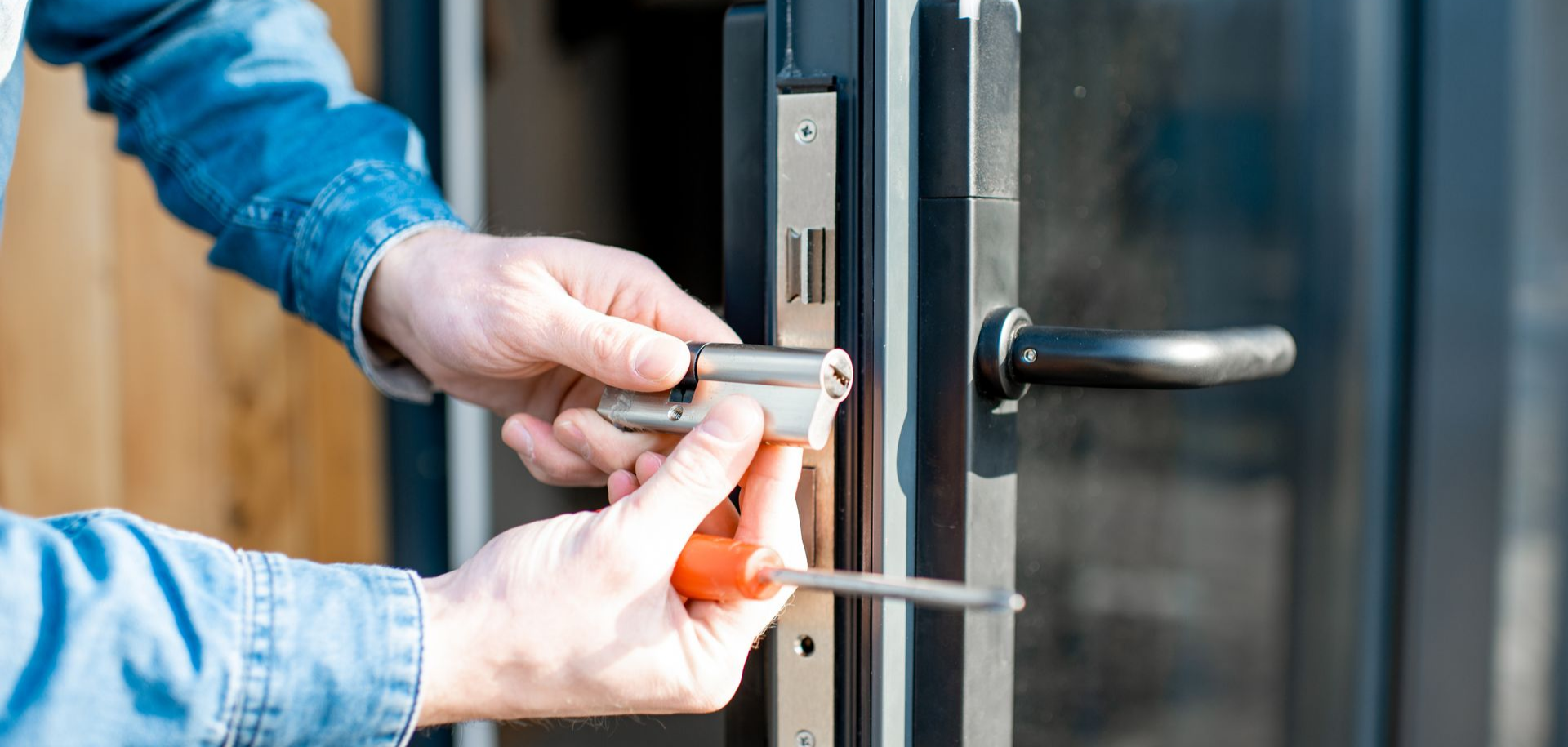 Personne installant une serrure de porte à l'aide d'un tournevis.