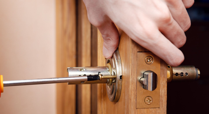 Personne utilisant un tournevis pour installer une serrure de porte sur une porte en bois.