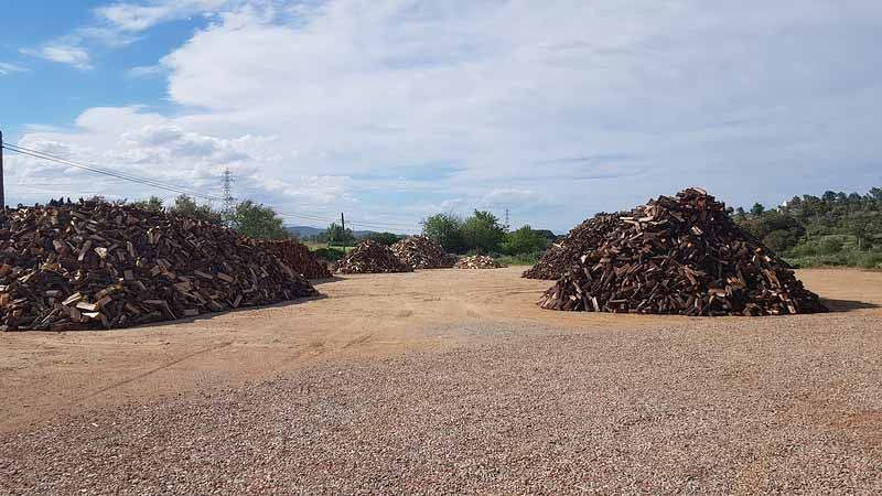 Piles de llenya tallada en un terreny de terra sota un cel ennuvolat.