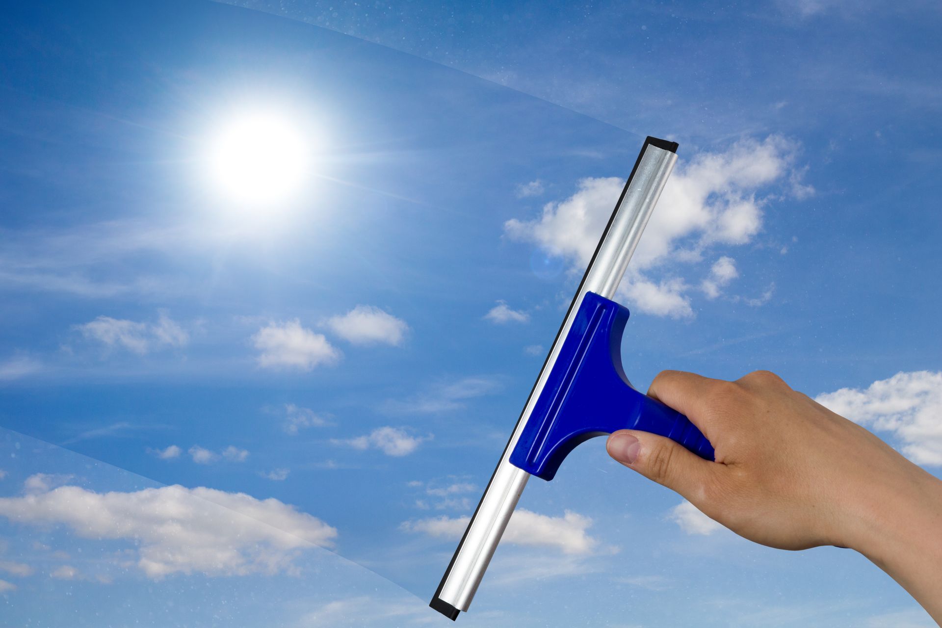 Eine Hand hält einen blau-silbernen Abzieher vor strahlendem Sonnenschein und blauem Himmel.