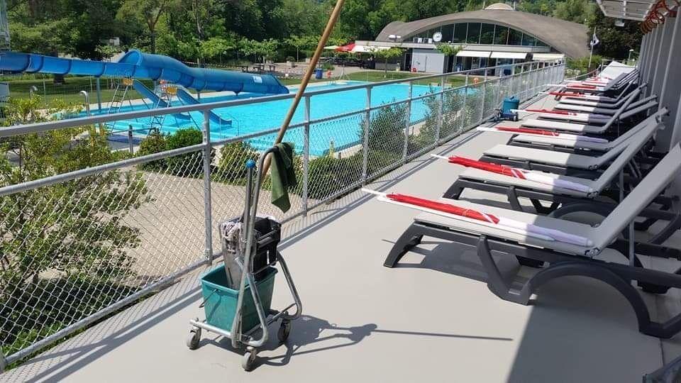 Blick auf den Pool mit Liegestühlen, Pool und Reinigungsutensilien. Blaue Wasserrutsche und umliegende Bäume. Sonniger Tag.