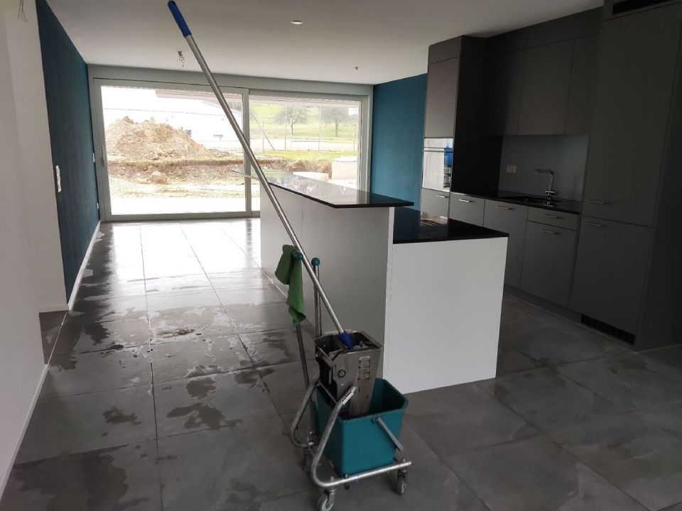 Putzeimer und Wischmopp auf nassem Fliesenboden in einer modernen, im Bau befindlichen Küche.